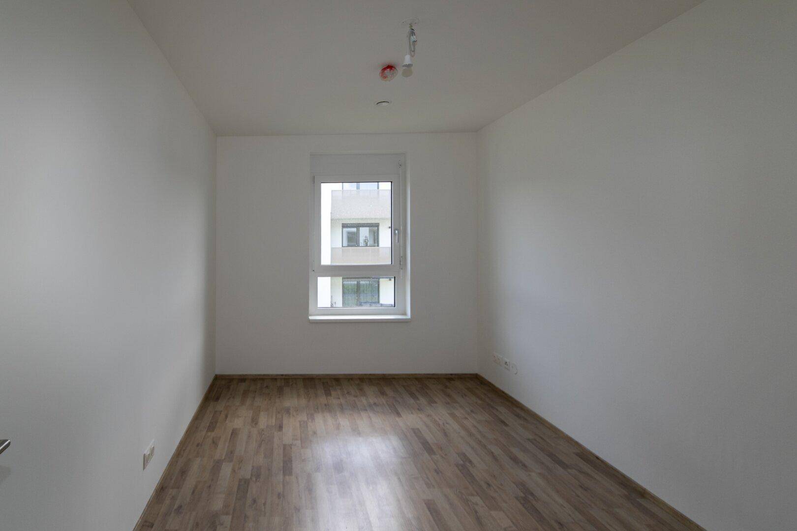 Helles Schlafzimmer mit Laminatboden und einem Fenster, das viel Tageslicht in den Raum lässt.