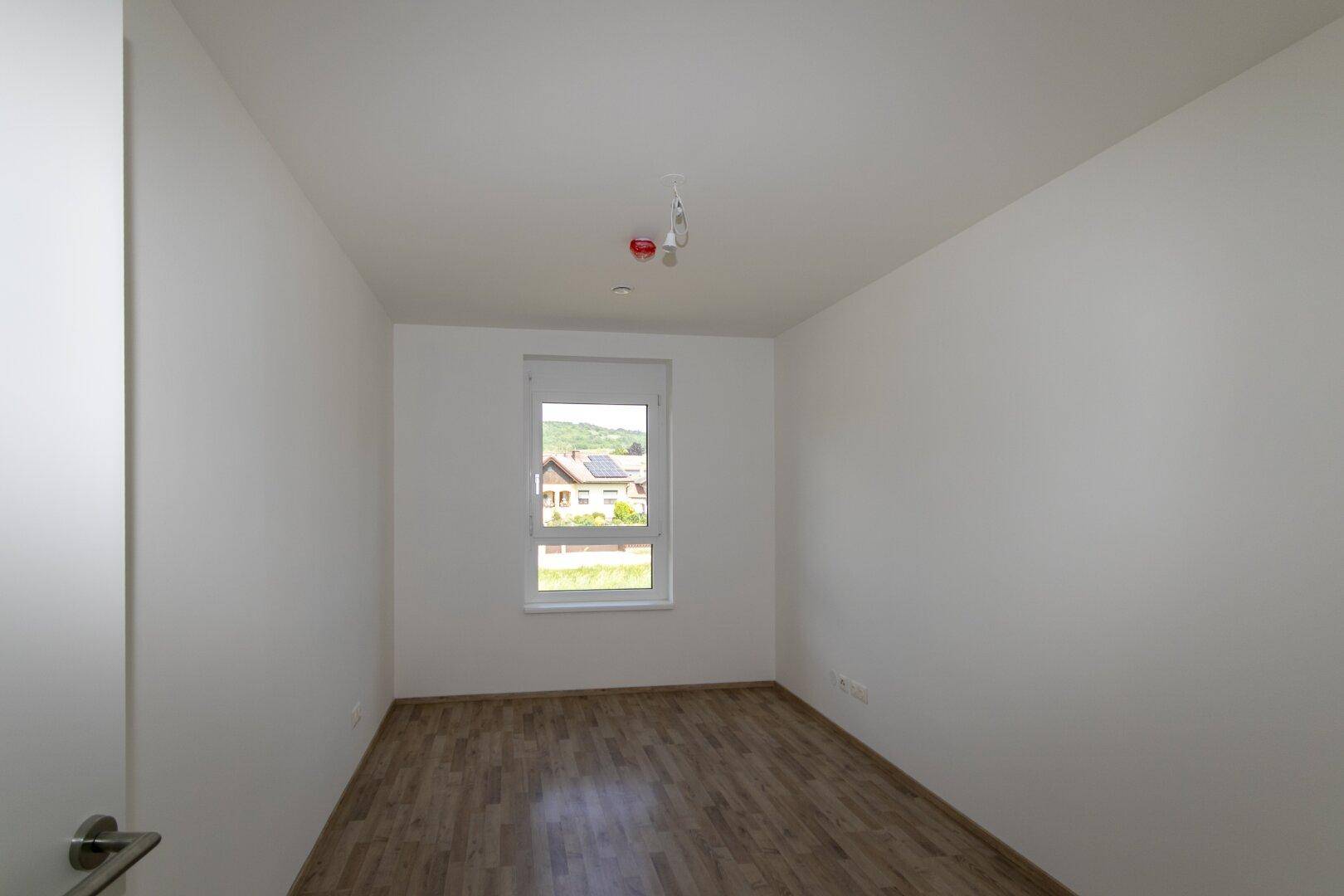 Helles Schlafzimmer mit Laminatboden und einem Fenster, das einen Blick ins Grüne bietet.