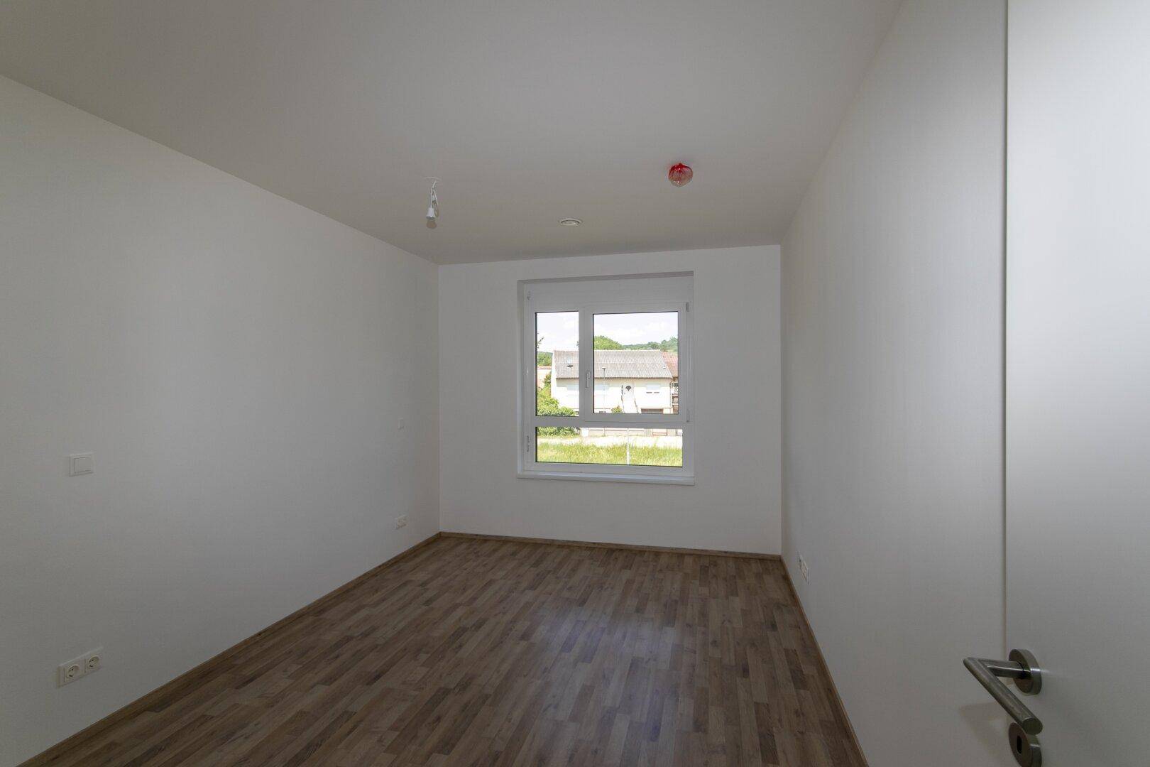 Geräumiges Schlafzimmer mit Laminatboden und weißen Wänden, ideal für individuelle Einrichtung.