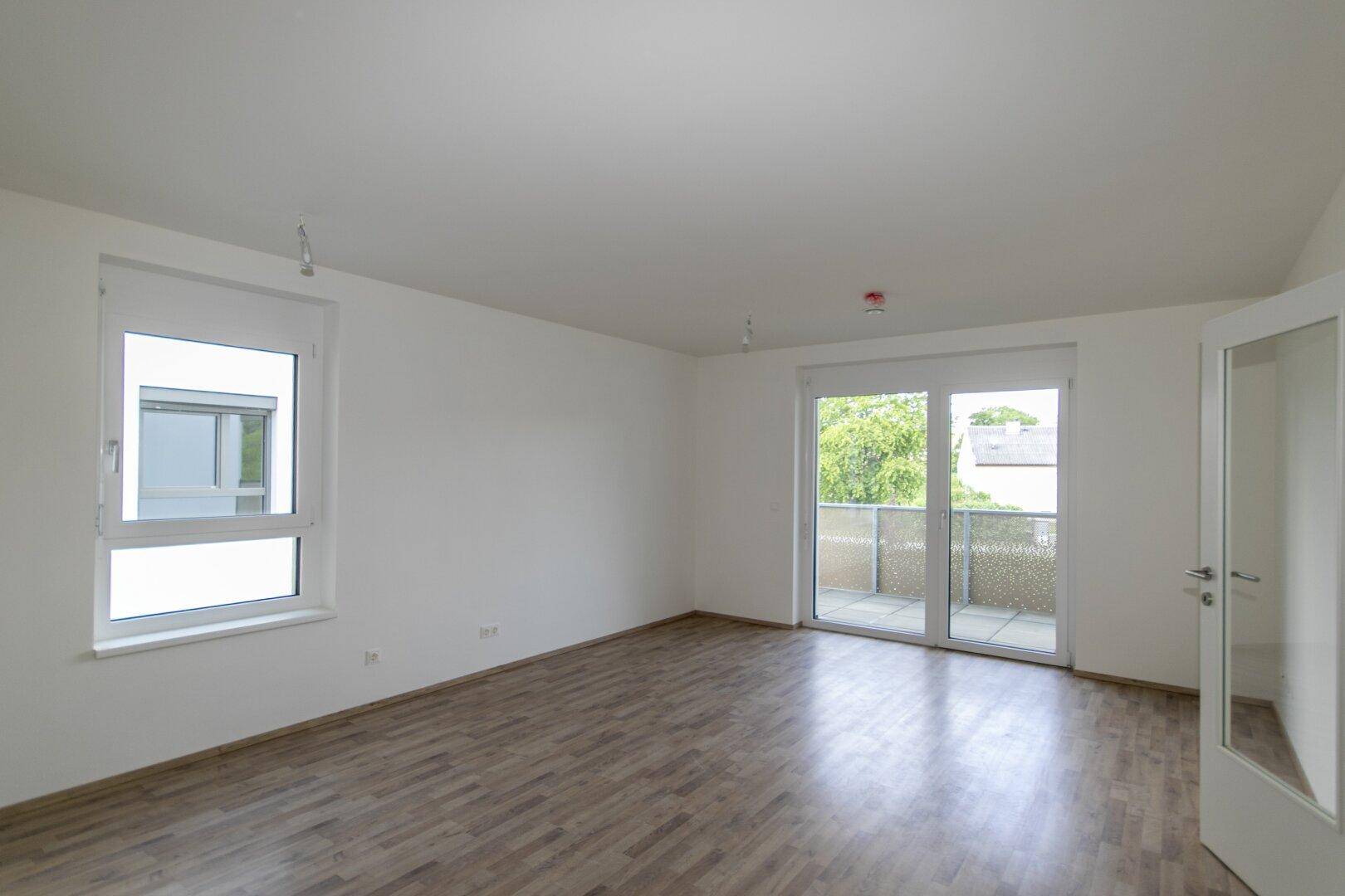 Geräumiges Wohnzimmer mit hellem Laminatboden und großen Fenstern für viel Tageslicht.