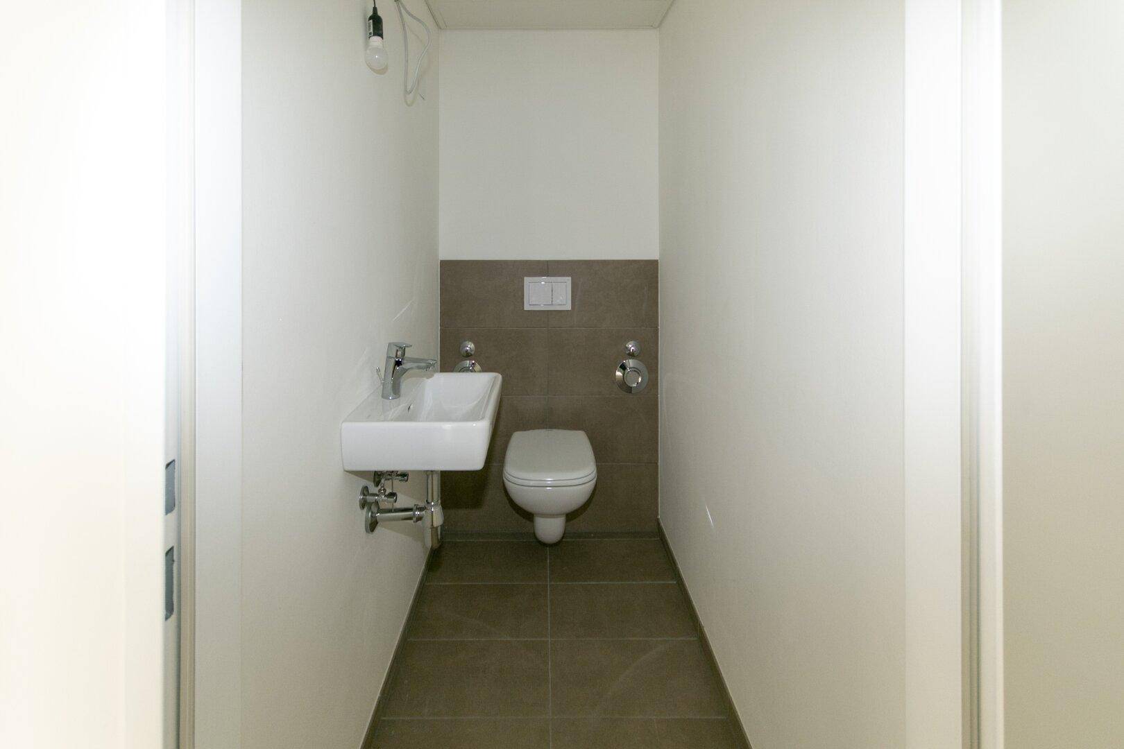 Separates Gäste-WC mit Wand-WC, kleinem Waschbecken und Fliesenboden.