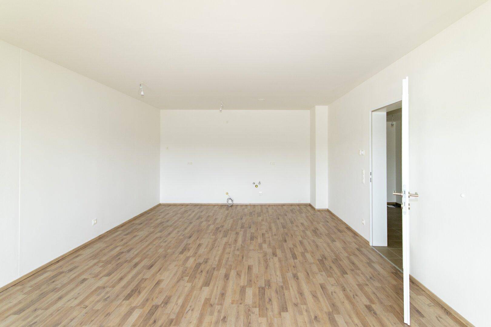 Geräumiges, unmöbliertes Zimmer mit Laminatboden und weißen Wänden, bereit zum Einzug.