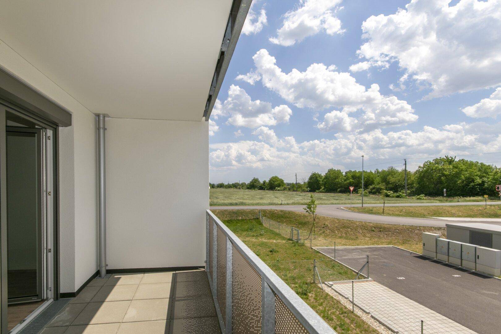 Sonniger Balkon mit Fliesenboden und weitem Blick über Felder und die Umgebung.