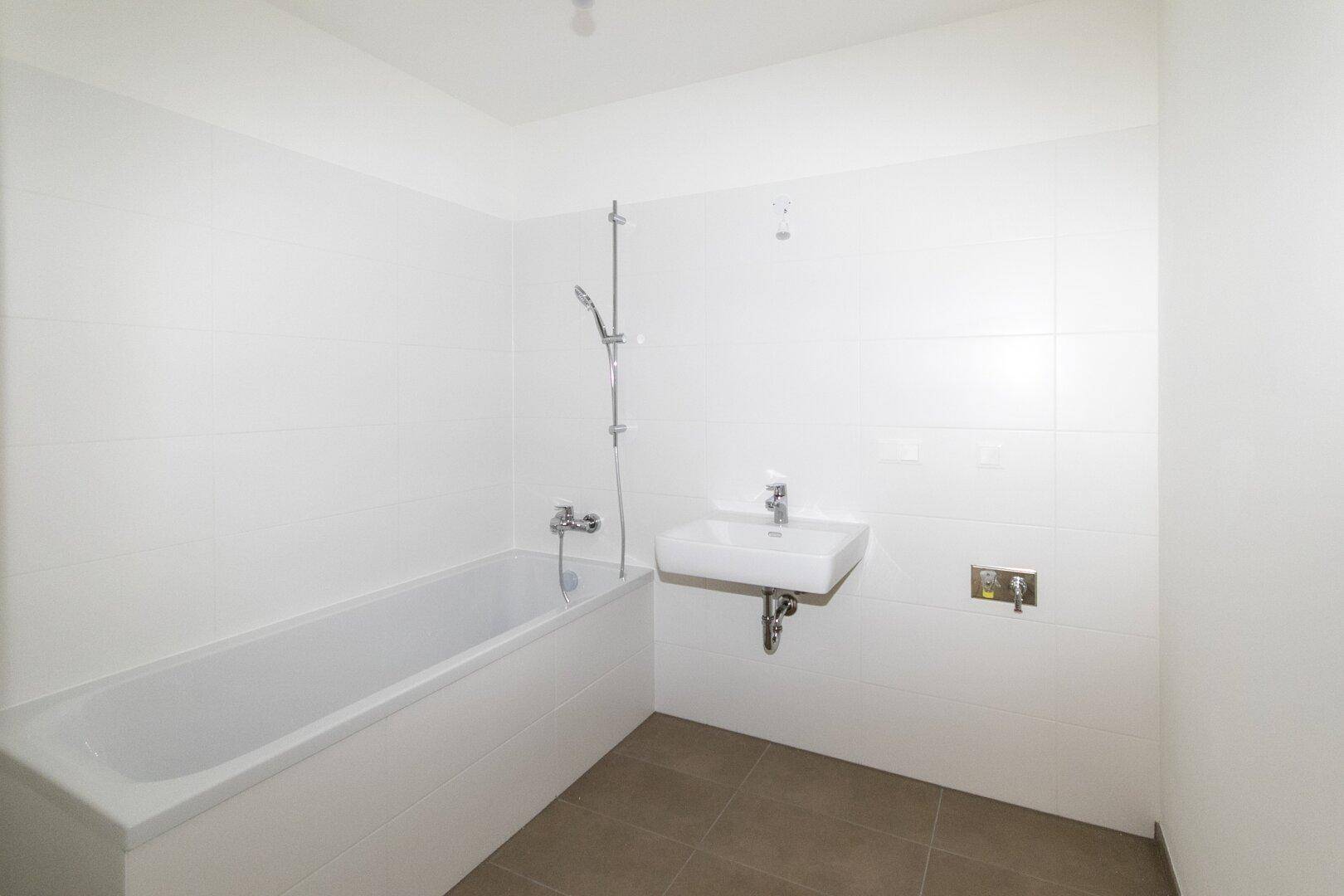 Modernes Badezimmer mit weißen Fliesen, Badewanne mit Duschfunktion und Einzelwaschbecken.