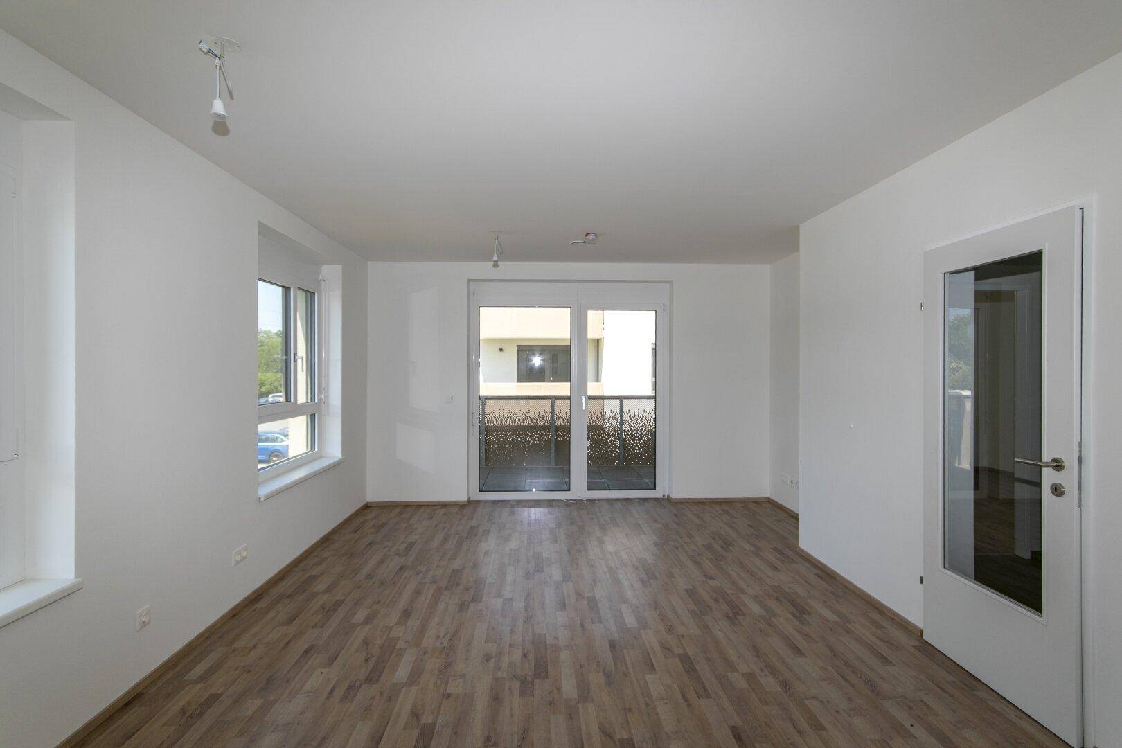 Geräumiges Wohnzimmer mit hellem Laminatboden und direktem Zugang zum Außenbereich.