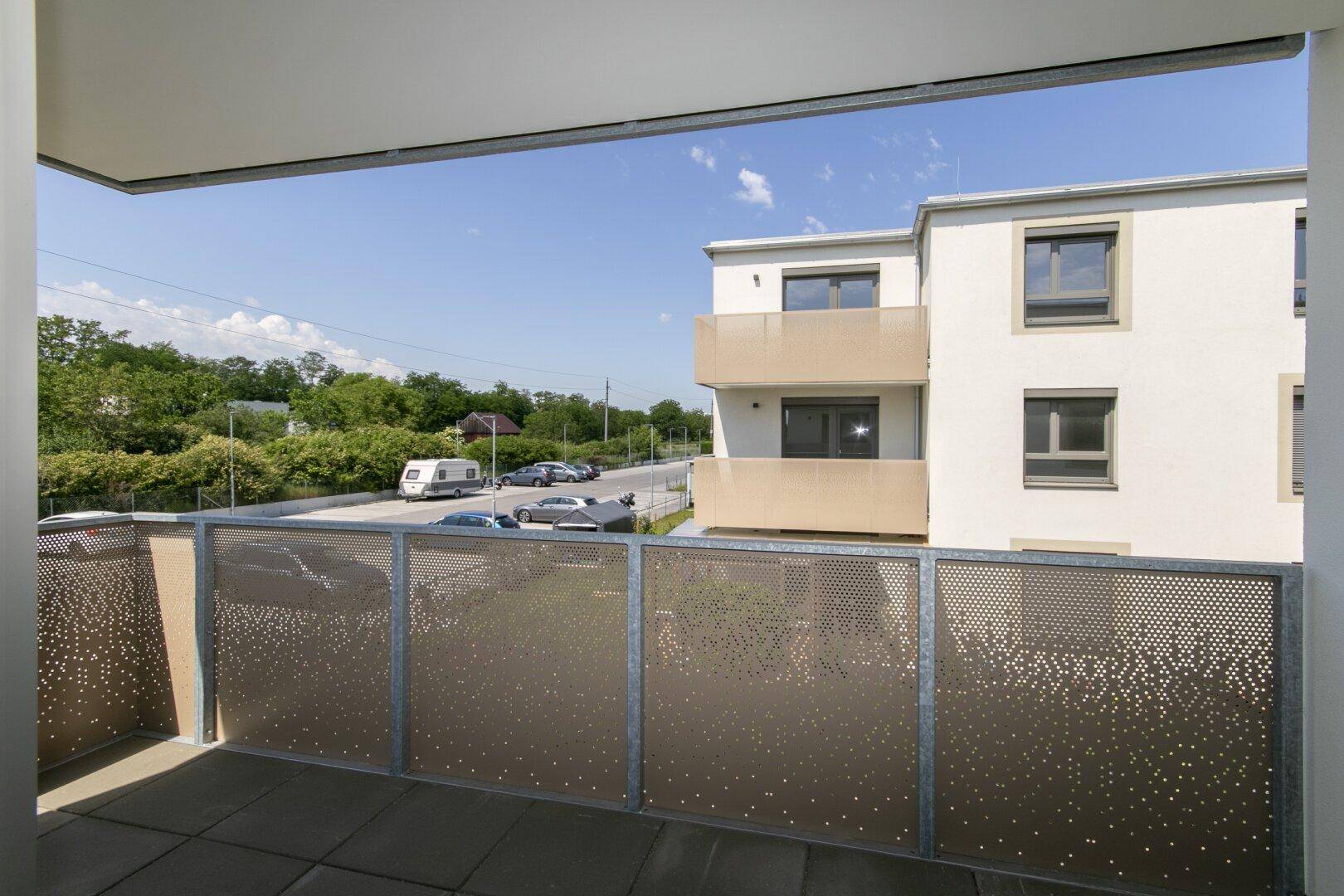 Heller Balkon mit Fliesenboden und Blick auf die umliegenden Neubauten und Parkplätze.