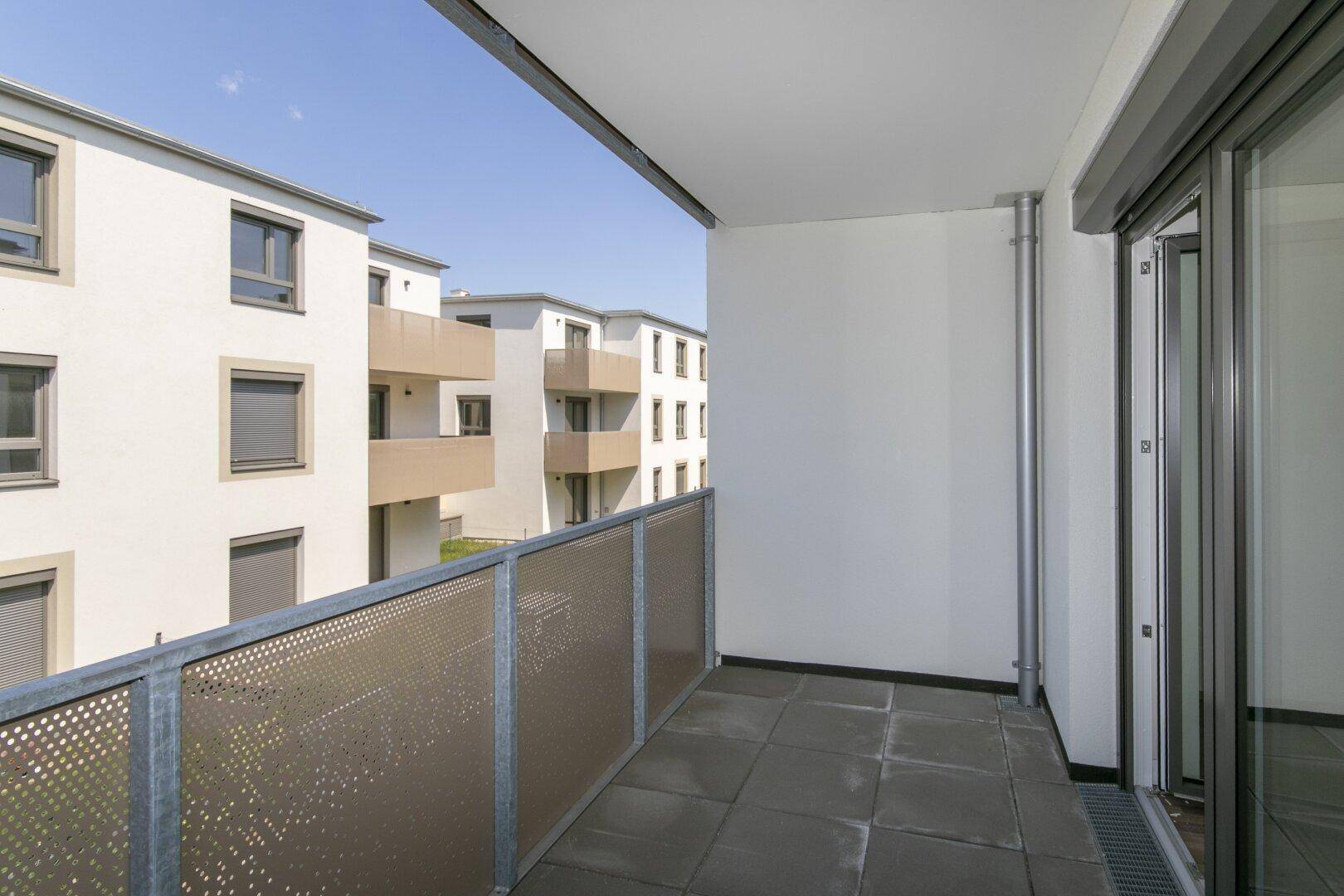 Geräumiger Balkon mit Fliesenboden und seitlichem Blick auf die moderne Wohnanlage.