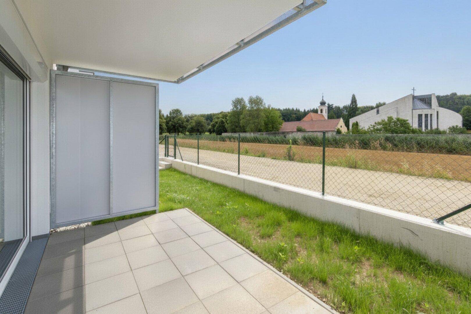 Helle Terrasse mit weitem Blick über Felder und auf entfernte Gebäude.