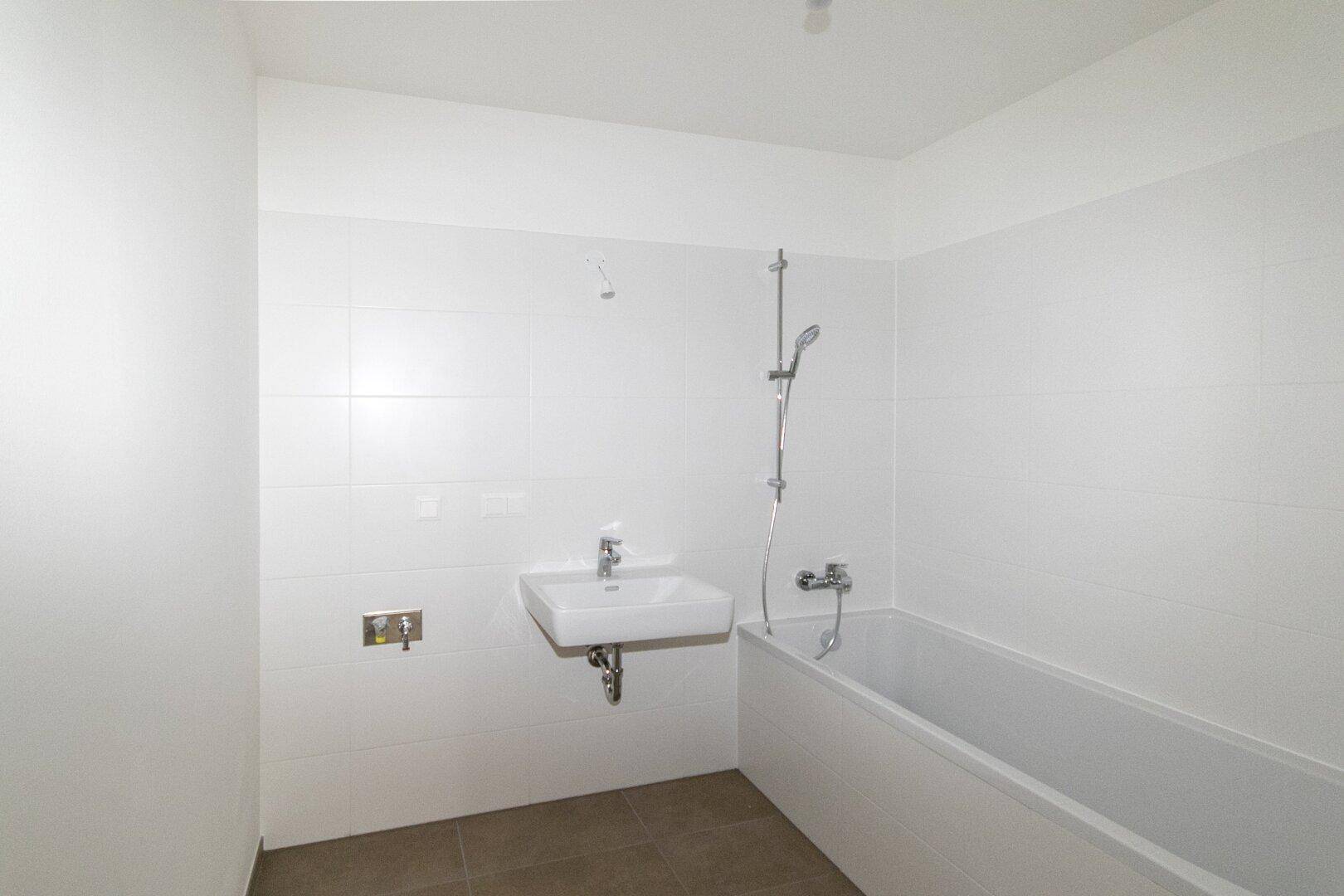 Modernes Badezimmer mit weißen Fliesen, Waschbecken und einer Badewanne, in neuwertigem Zustand.