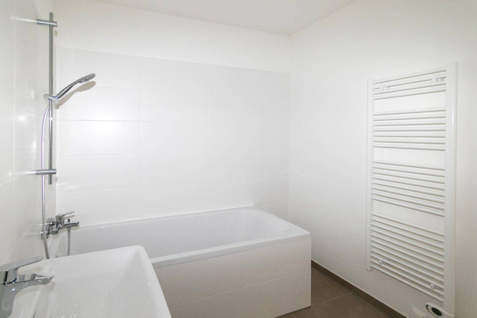 Helles Badezimmer mit Badewanne, Waschbecken und einem praktischen Handtuchheizkörper.