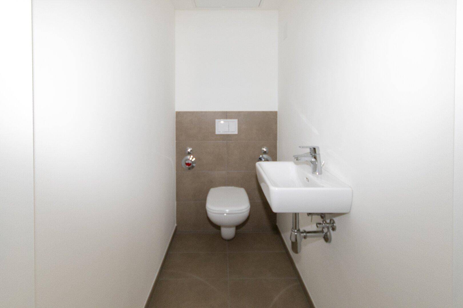 Separates Gäste-WC mit wandhängender Toilette und kleinem Waschbecken, modern gefliest.