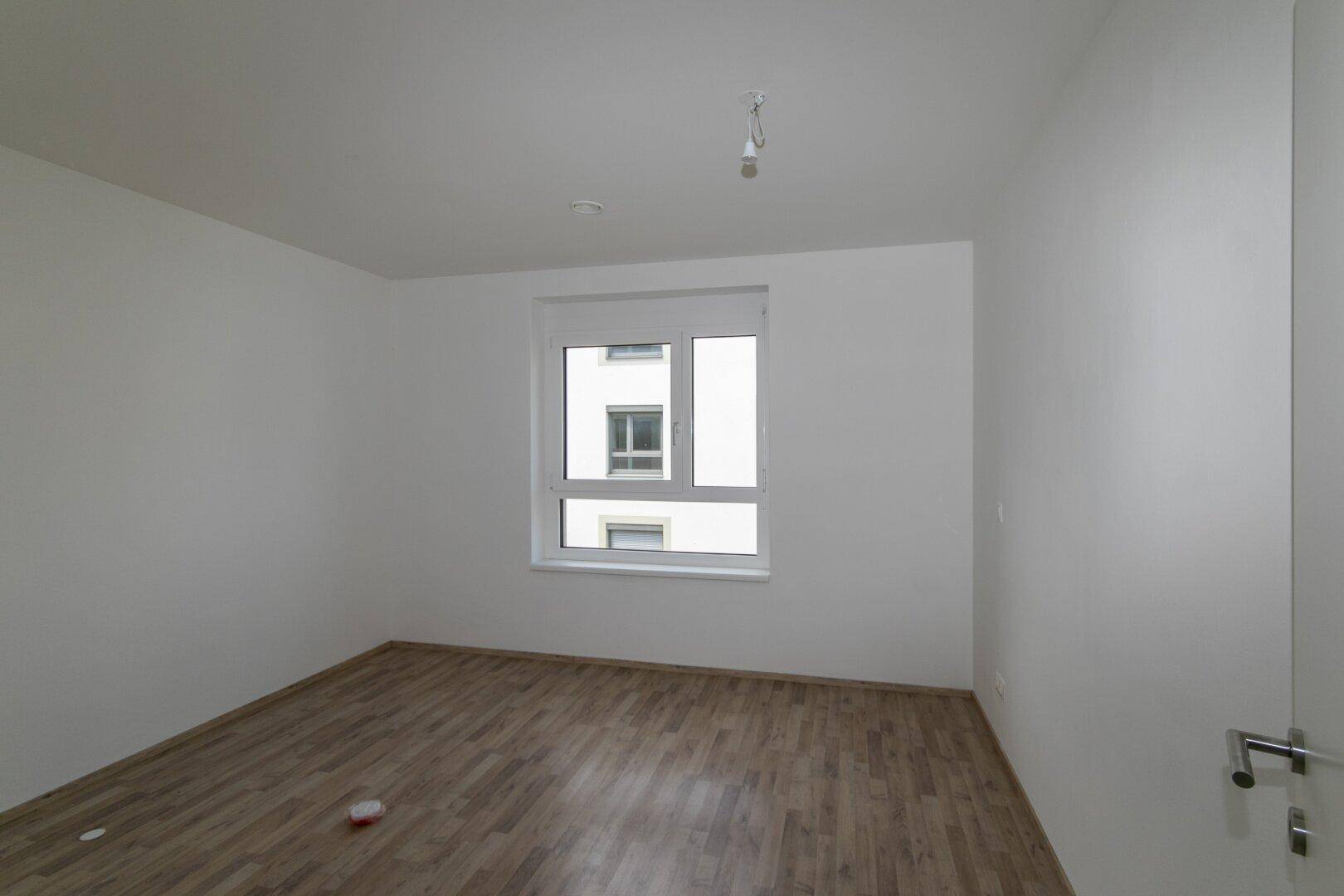 Unmöbliertes Schlafzimmer mit hellem Holzboden und einem Fenster, das viel Tageslicht hereinlässt.