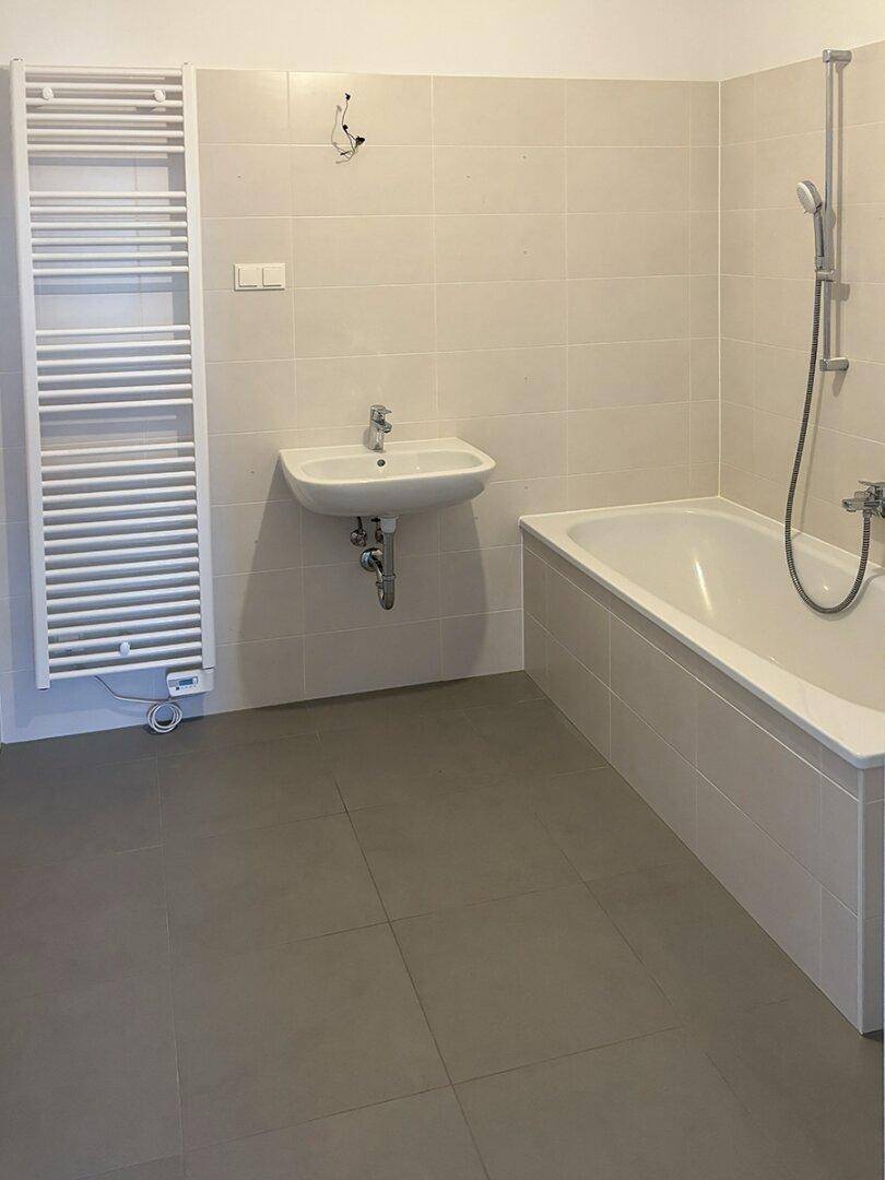 Helles Badezimmer mit Badewanne, Waschbecken und beheiztem Handtuchhalter.