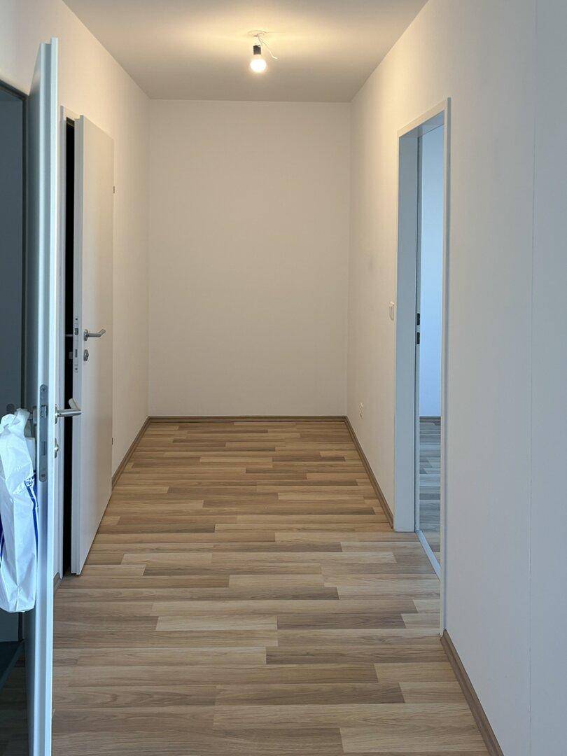 Schmaler, heller Flur mit Laminatboden und weißen Wänden.