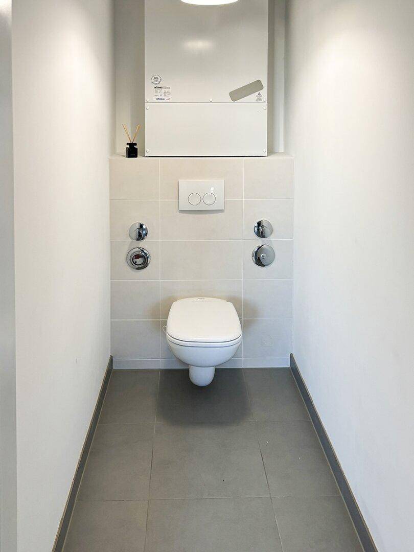 Modernes Gäste-WC mit Wand-WC und grauen Bodenfliesen.