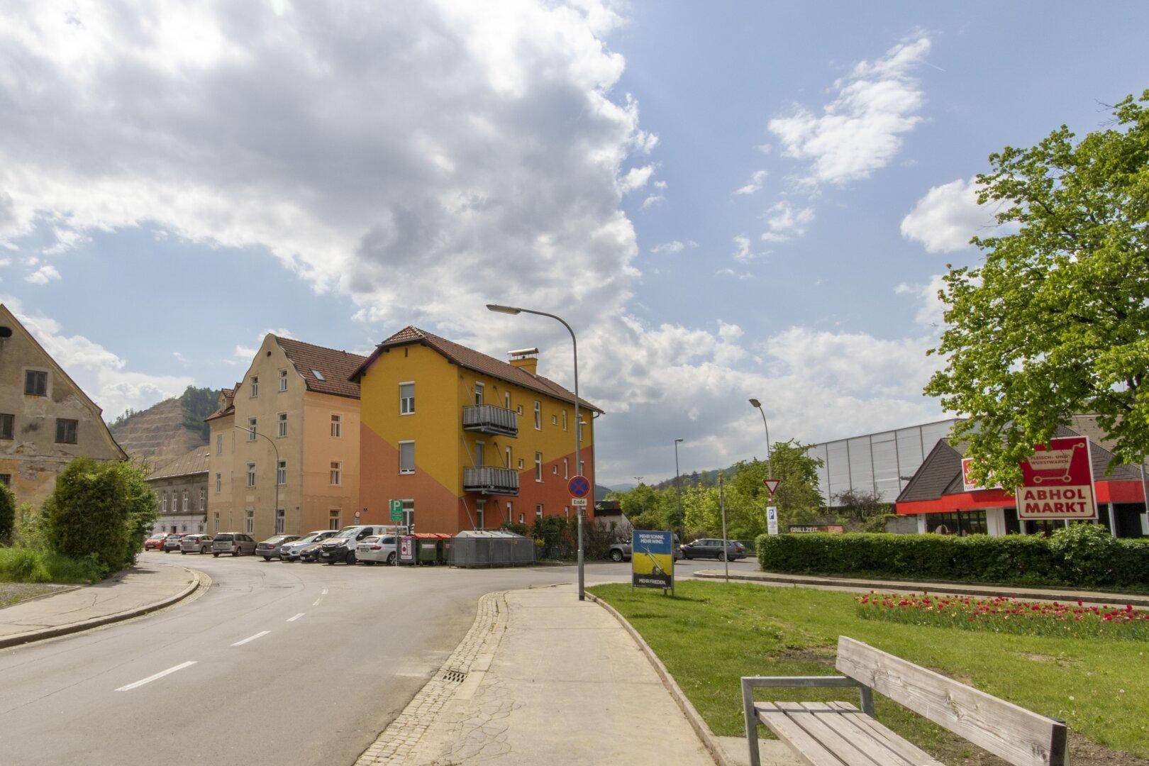 Weitläufige Ansicht der Umgebung mit dem farbigen Gebäude, weiteren Häusern und einem Markt.