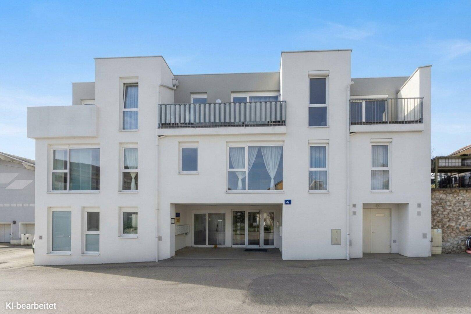 Moderne Wohnanlage mit weißer Fassade, großen Fenstern und Balkonen, in einer städtischen Umgebung.