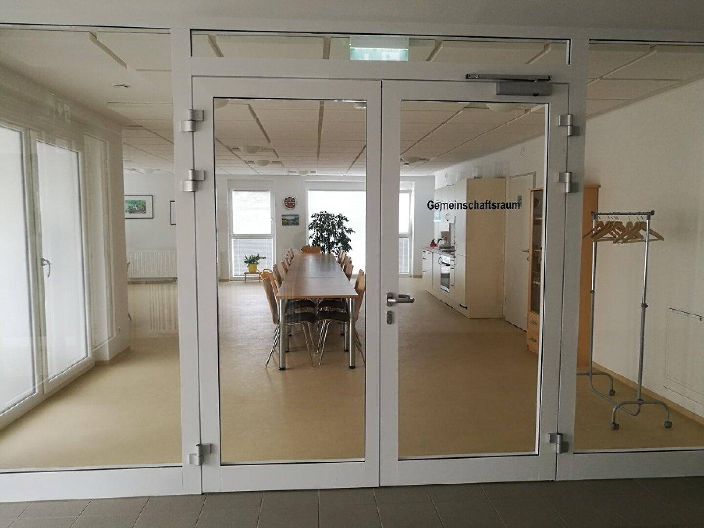 Heller Gemeinschaftsraum mit Esstisch und offener Küche, ideal für soziale Zusammenkünfte.