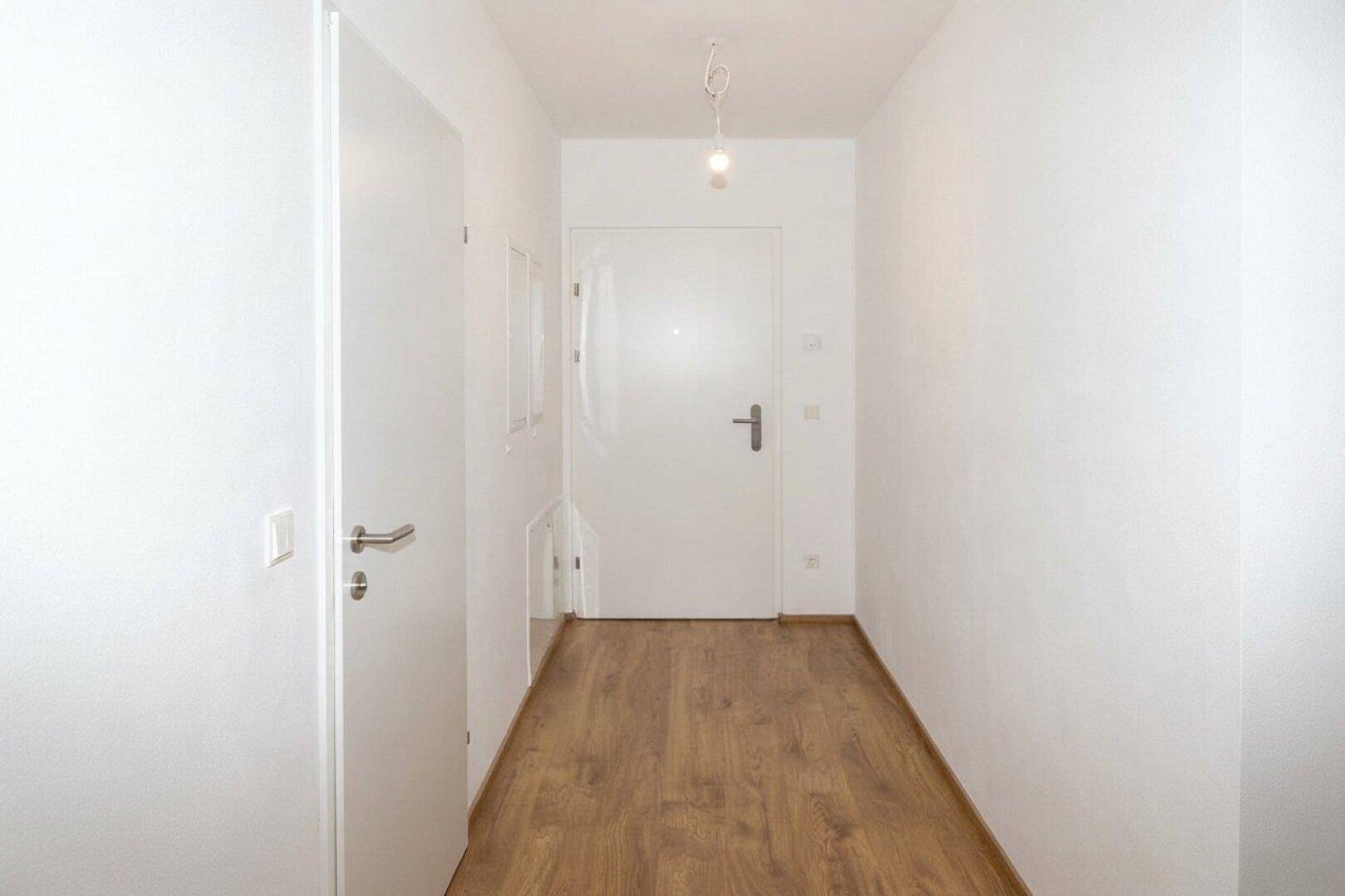 Heller Flur mit Laminatboden und weißen Wänden, der zu verschiedenen Räumen führt.
