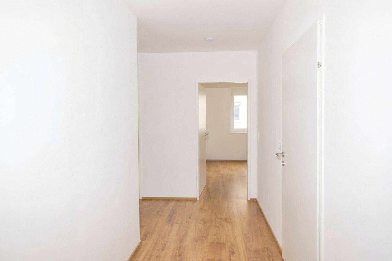 Schmaler, heller Flur mit Laminatboden und weißen Wänden, verbindet die Wohnbereiche.
