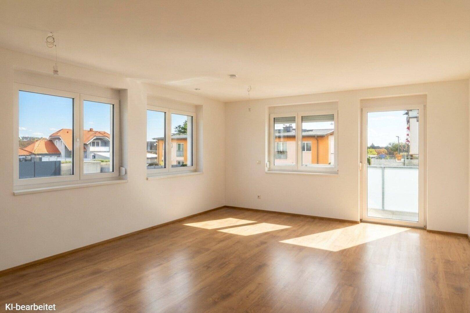 Helles, leeres Zimmer mit Laminatboden und mehreren Fenstern, inklusive Balkonzugang.