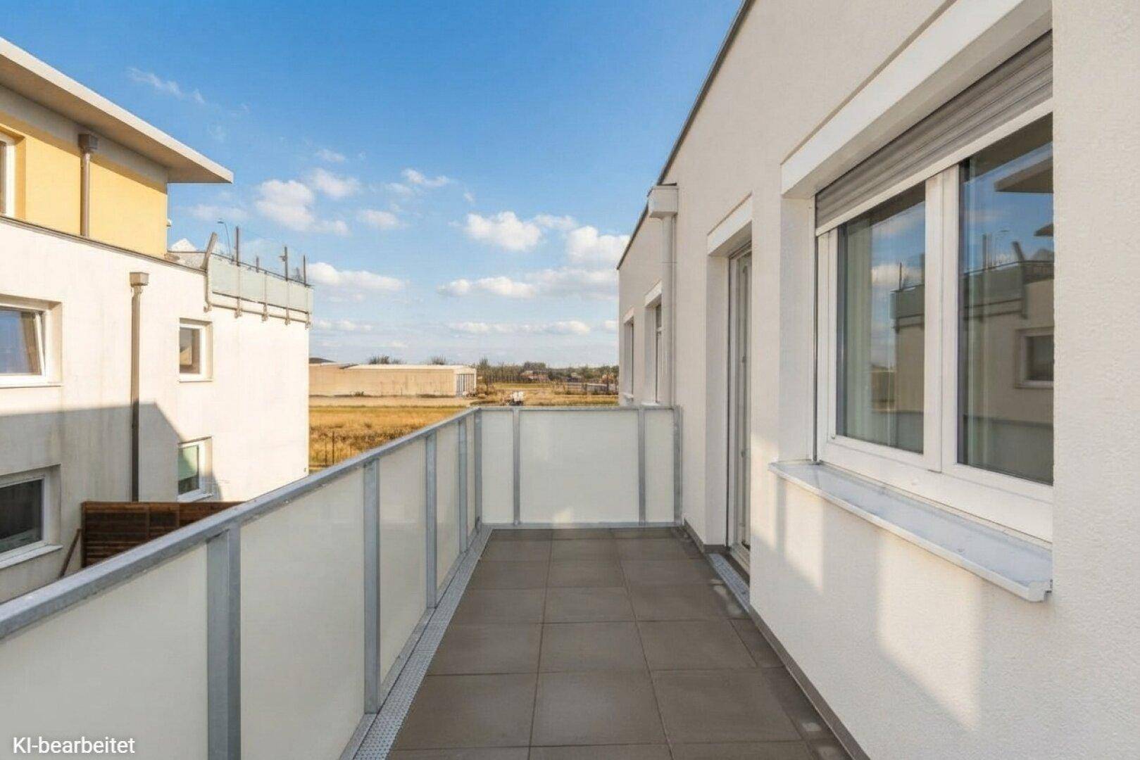 Langer Balkon mit Fliesenboden und Glasbrüstung, bietet weite Aussicht auf die Umgebung.