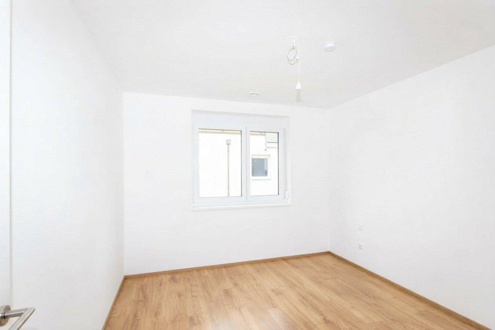Helles Zimmer mit Laminatboden und weißen Wänden, ideal als Schlaf- oder Arbeitszimmer.