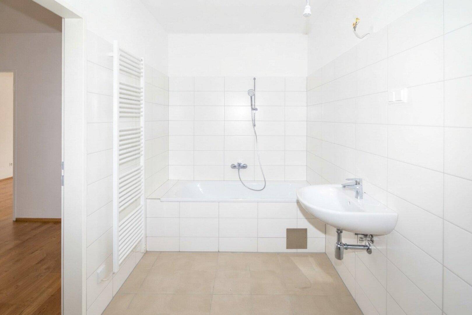 Modern gefliestes Badezimmer mit Badewanne, Duscharmatur und praktischem Handtuchheizkörper.