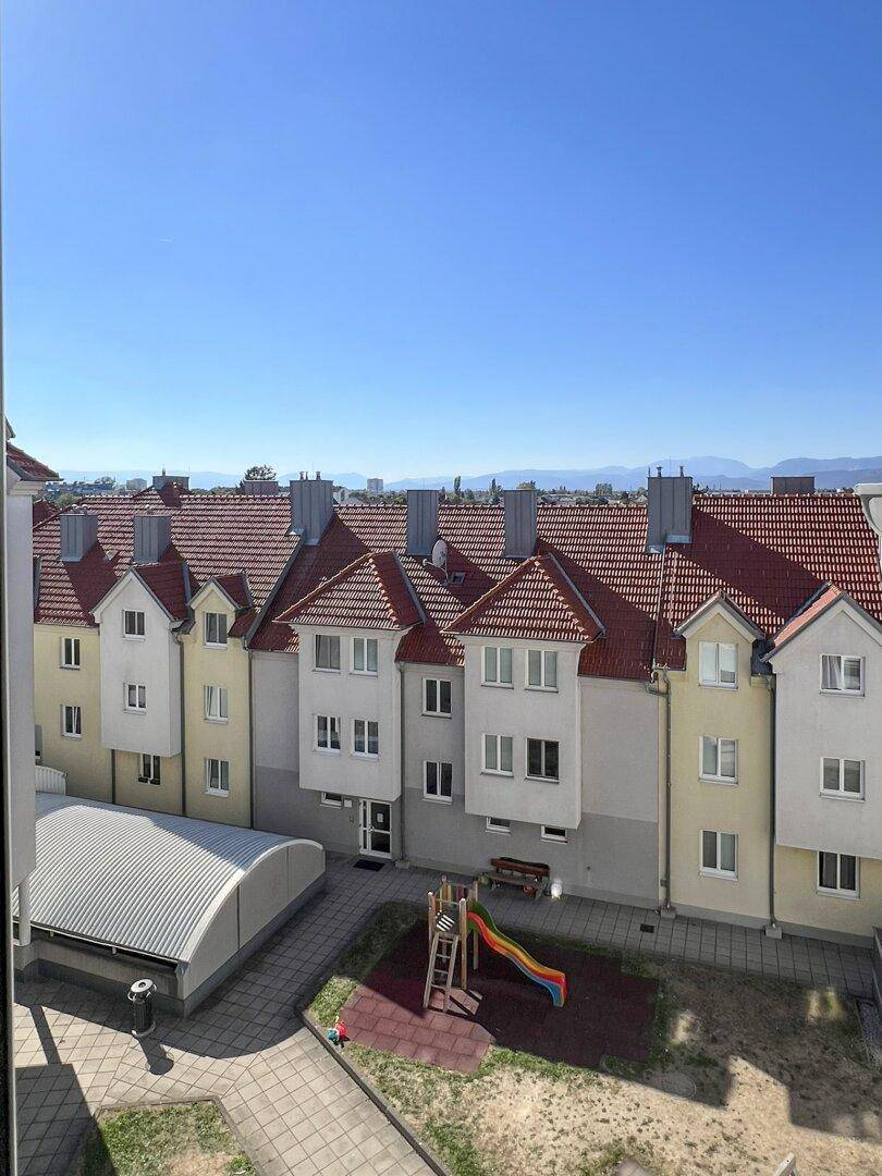 Blick aus dem Fenster auf einen sonnigen Innenhof mit Spielplatz und weiteren Wohngebäuden.