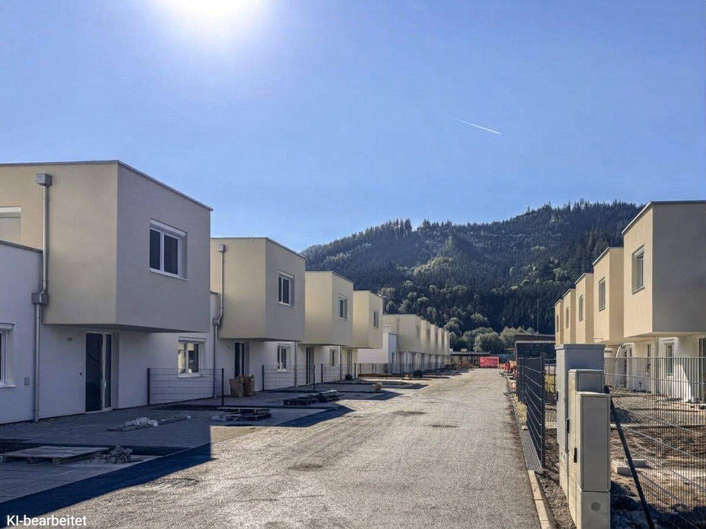 Reihenhäuser in sonniger Lage mit Blick auf bewaldete Berge und neue Infrastruktur.