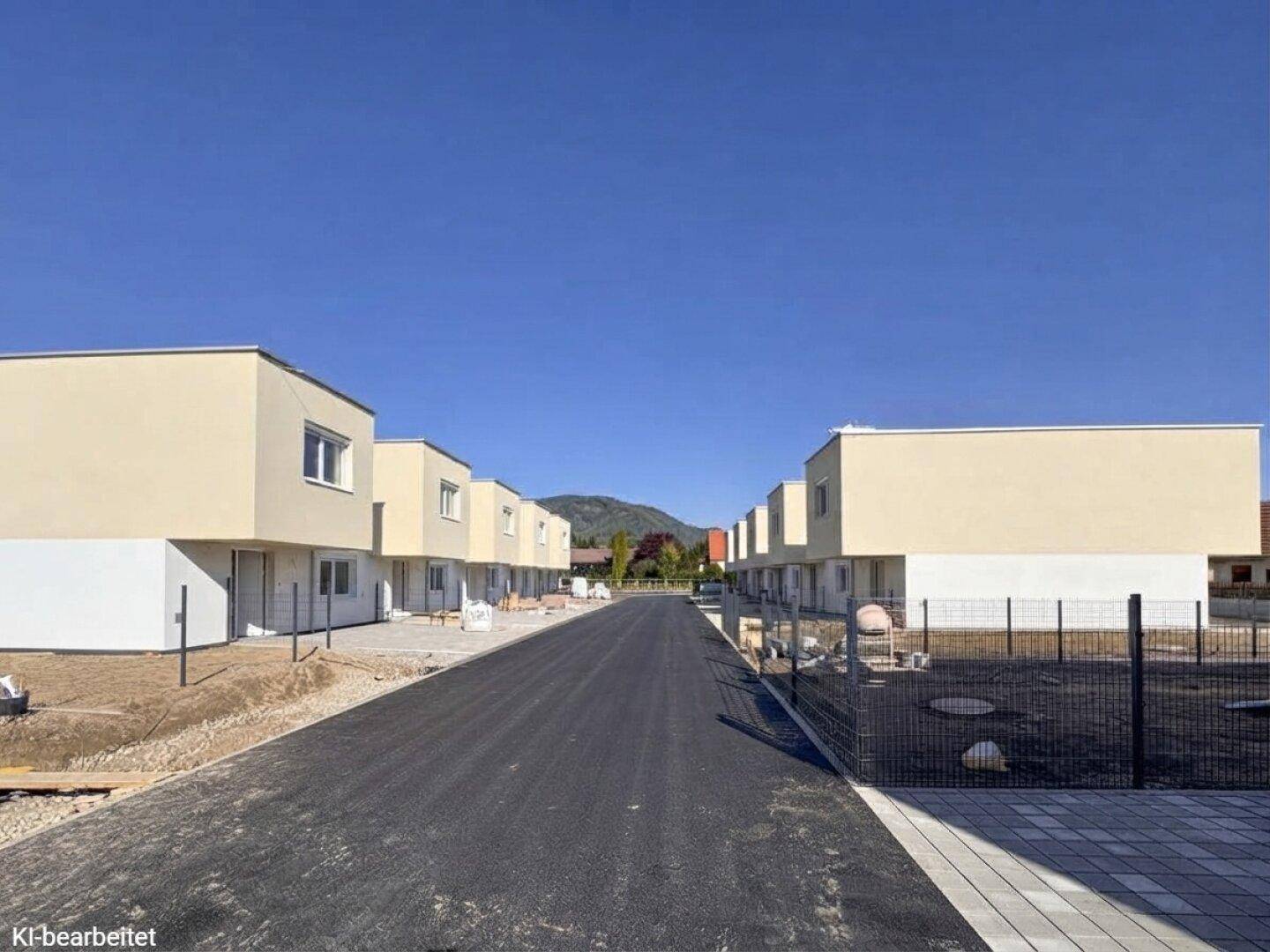 Neue Wohnsiedlung mit modernen Reihenhäusern und Blick auf die umliegende Berglandschaft.