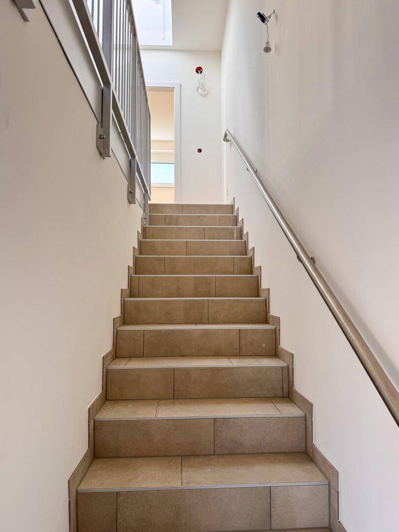 Modernes Treppenhaus mit Fliesenboden, Metallgeländer und hellem Anstrich.