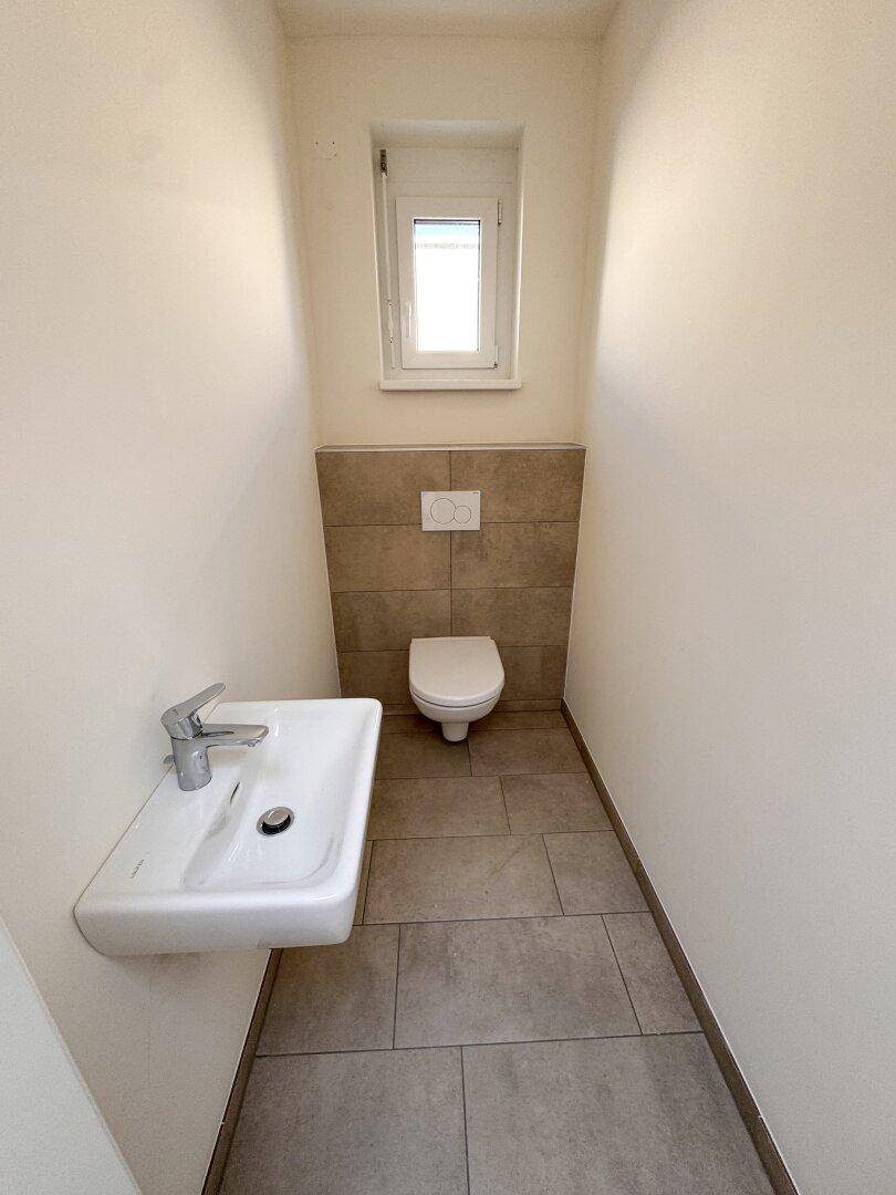 Separates Gäste-WC mit wandhängender Toilette, kleinem Waschbecken und Fenster.
