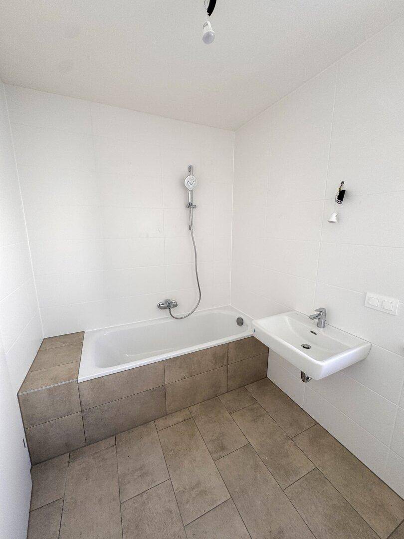 Modernes Badezimmer mit Badewanne, Dusche und Einzelwaschbecken, hell gefliest.