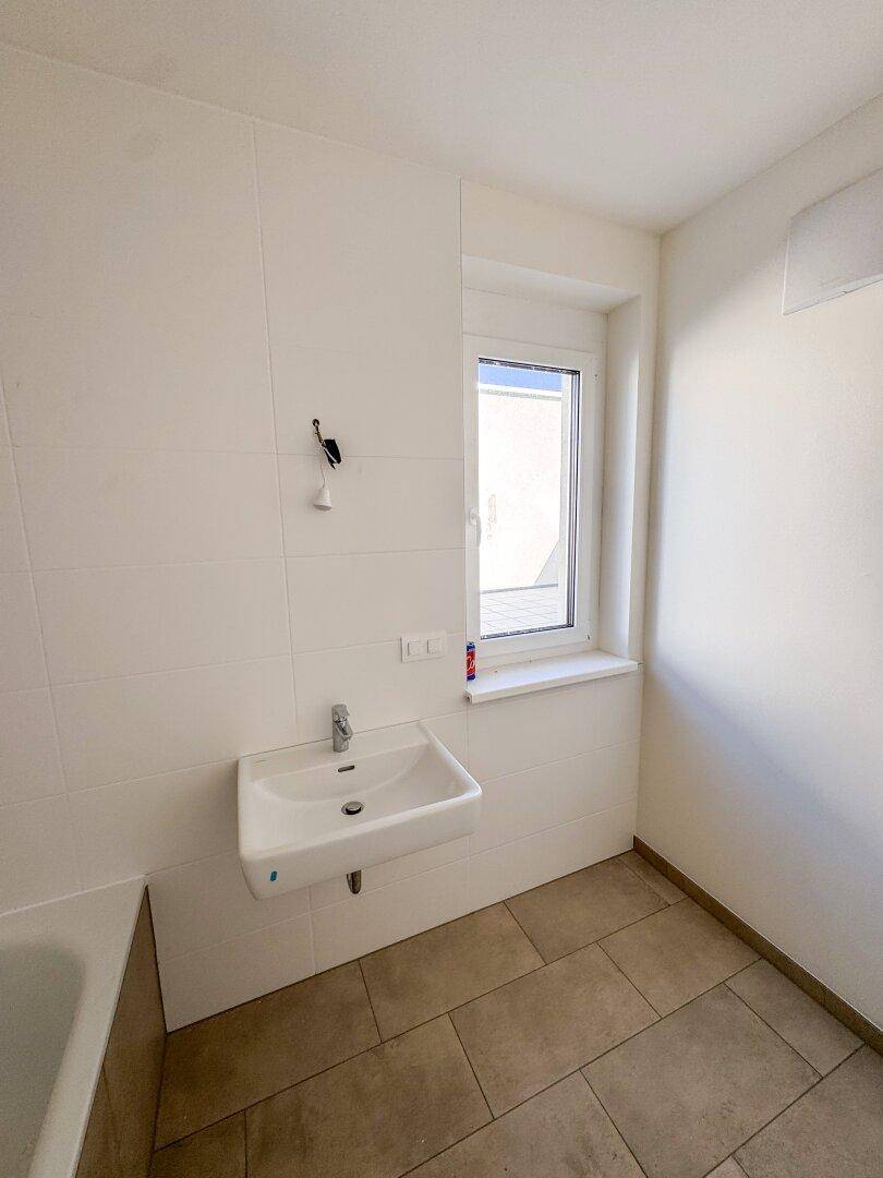 Helles Badezimmer mit Einzelwaschbecken, Fenster und modernen Fliesen an Wänden und Boden.
