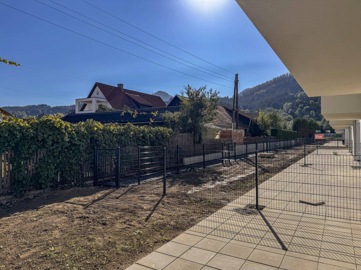 Neu angelegter Gartenbereich mit Zaun und Blick auf die grüne Umgebung und Berge.
