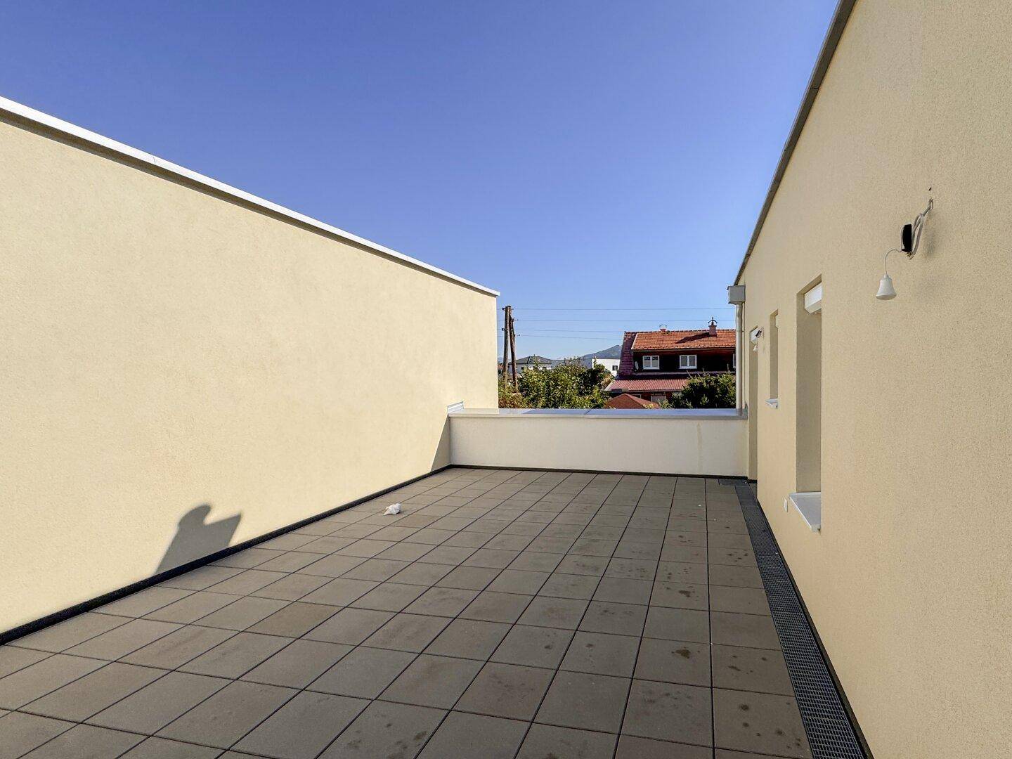 Große, geflieste Dachterrasse mit viel Platz und weitem Blick unter blauem Himmel.