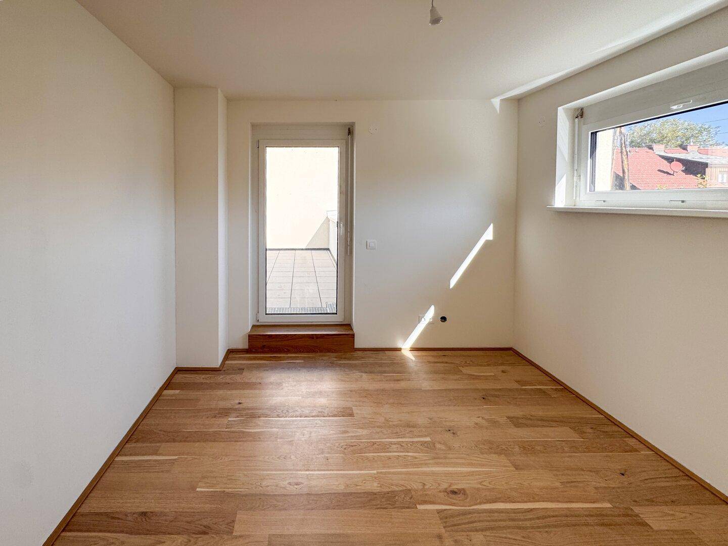 Helles Schlafzimmer mit Holzboden, Fenster und direktem Zugang zu einer sonnigen Terrasse.