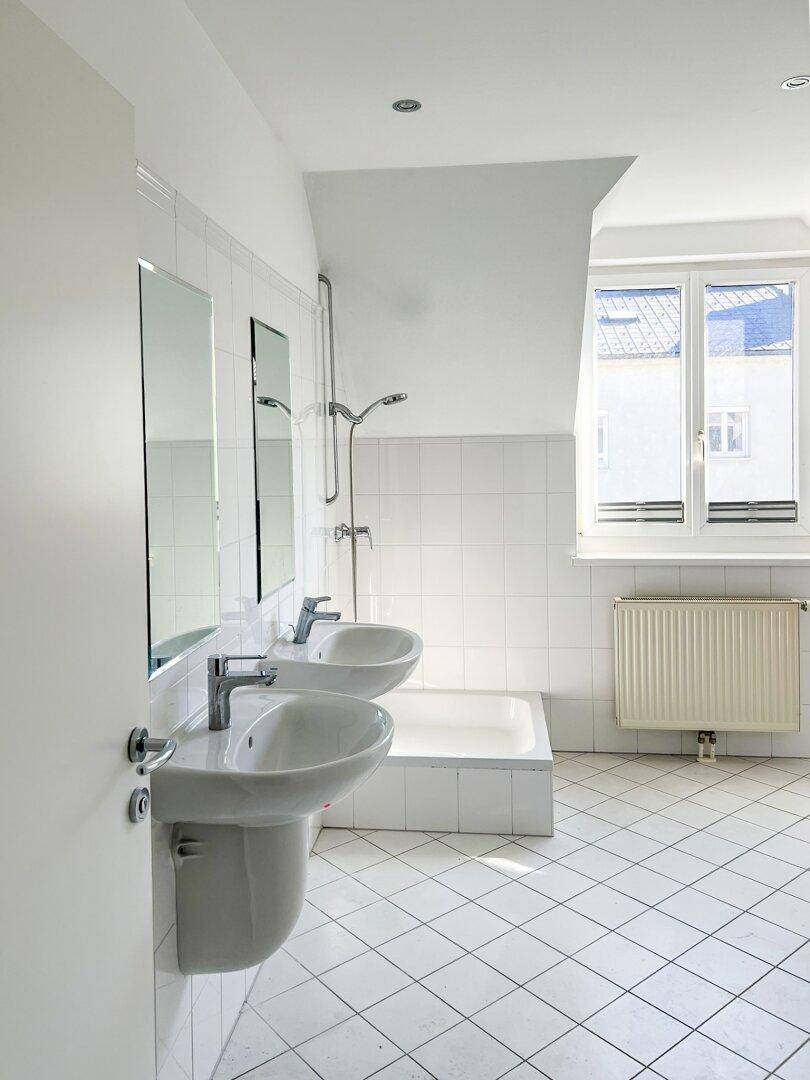 Geräumiges Badezimmer im Dachgeschoss mit zwei Waschbecken, Badewanne und weißen Fliesen.