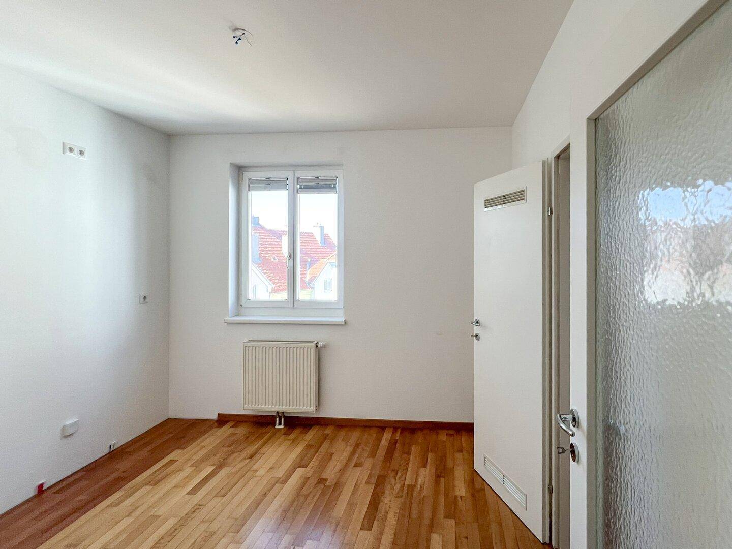 Unmöbliertes Schlafzimmer mit Parkettboden, einem Fenster und viel Tageslicht.
