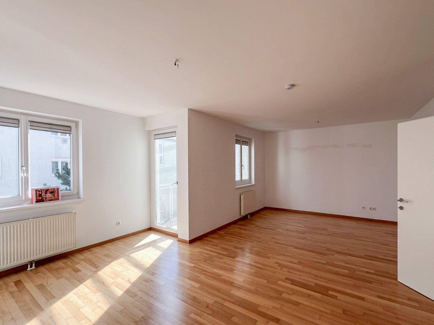 Geräumiges, helles Zimmer mit Holzboden und Zugang zu einem möglichen Balkon oder einer Terrasse.