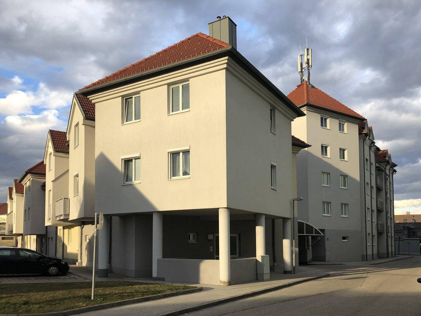 Wohngebäude mit heller Fassade, roten Ziegeldächern und Säulen im Eingangsbereich bei Sonnenuntergang.