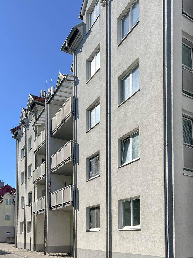 Moderne Fassade eines Mehrfamilienhauses mit Balkonen und vielen Fenstern unter blauem Himmel.