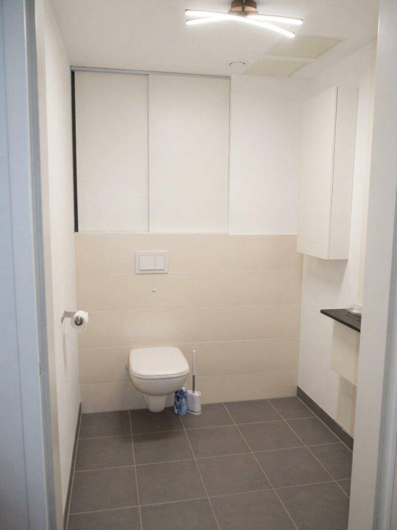 Separate Gästetoilette mit Wand-WC, kleinem Waschbecken und dunklem Fliesenboden.