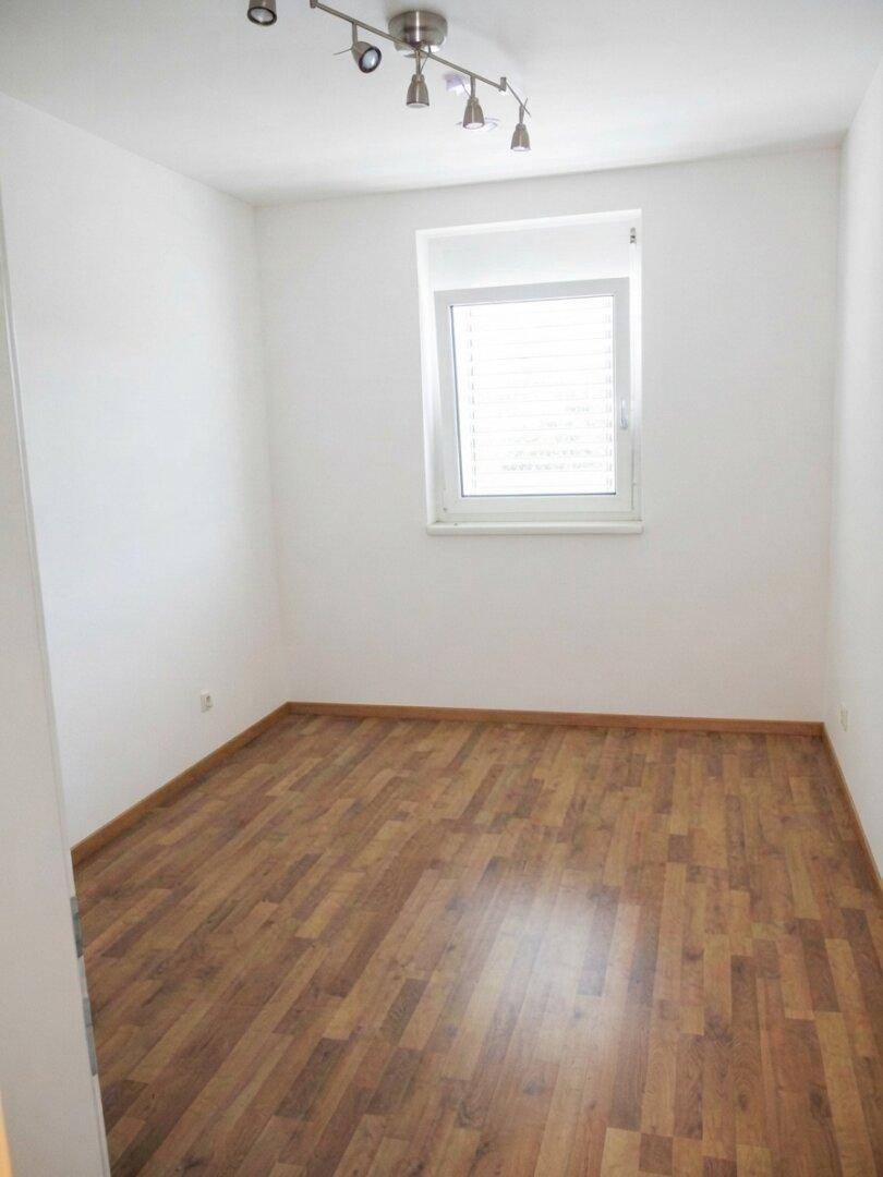 Helles Zimmer mit Laminatboden und einem Fenster, vielseitig nutzbar als Schlaf- oder Arbeitszimmer.