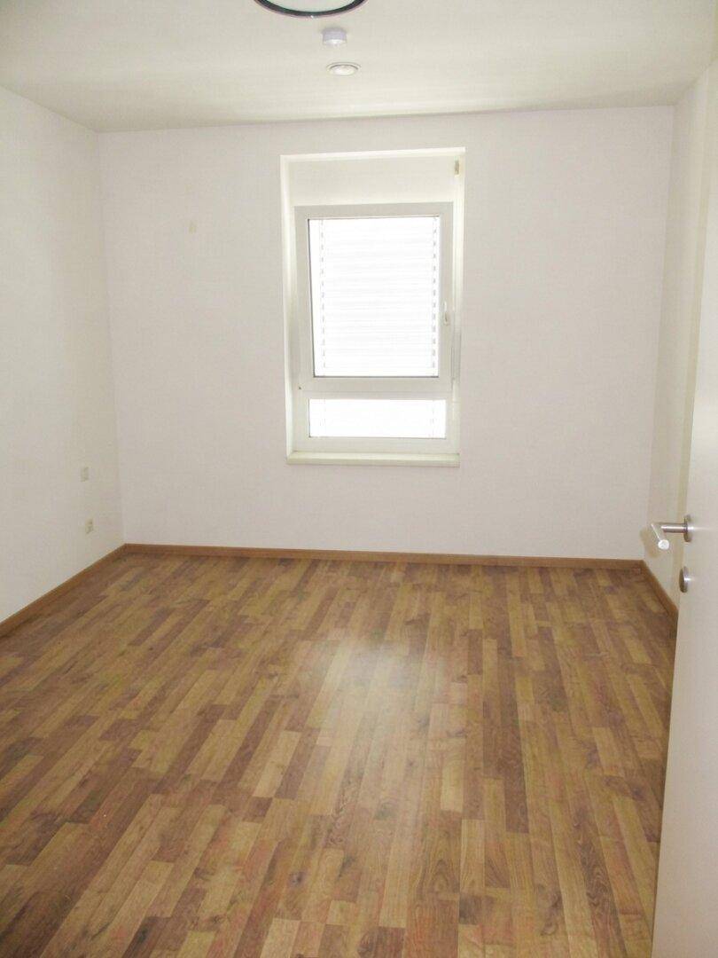 Freundliches Zimmer mit Laminatboden und großem Fenster, das viel Tageslicht hereinlässt.