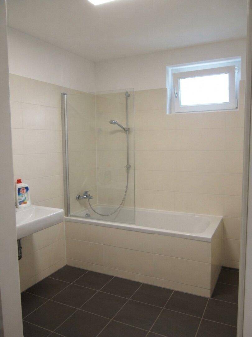 Modernes Badezimmer mit Badewanne, Duschabtrennung, Waschbecken und einem Fenster für natürliche Belüftung.