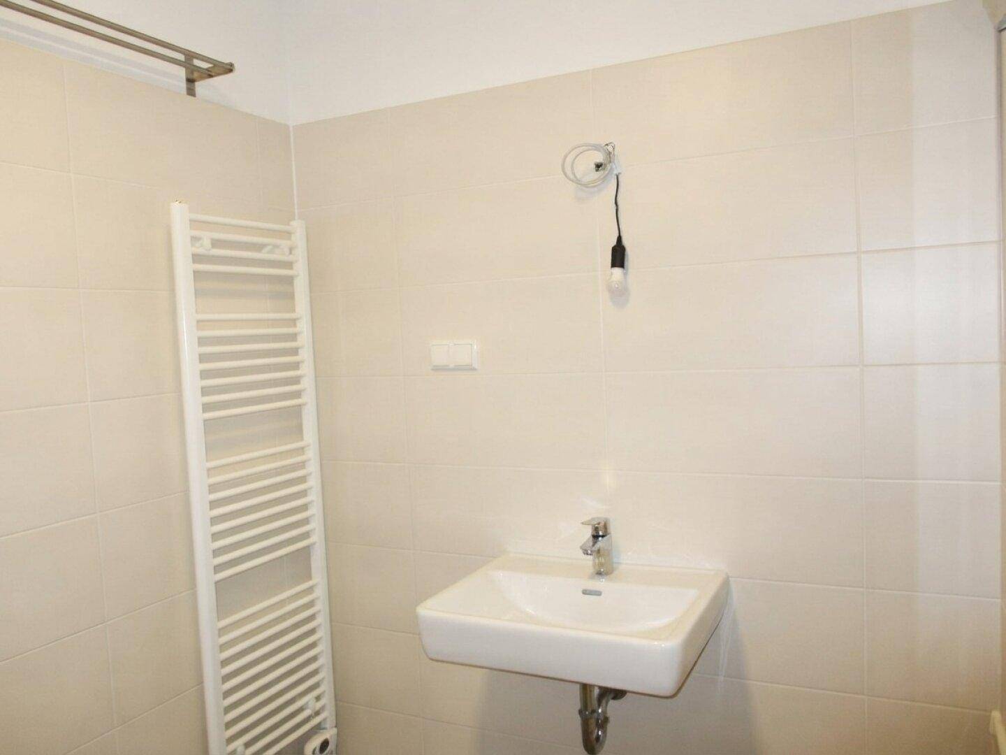 Badezimmerdetail mit Waschbecken, beheiztem Handtuchhalter und hellen Fliesen, funktional und sauber.