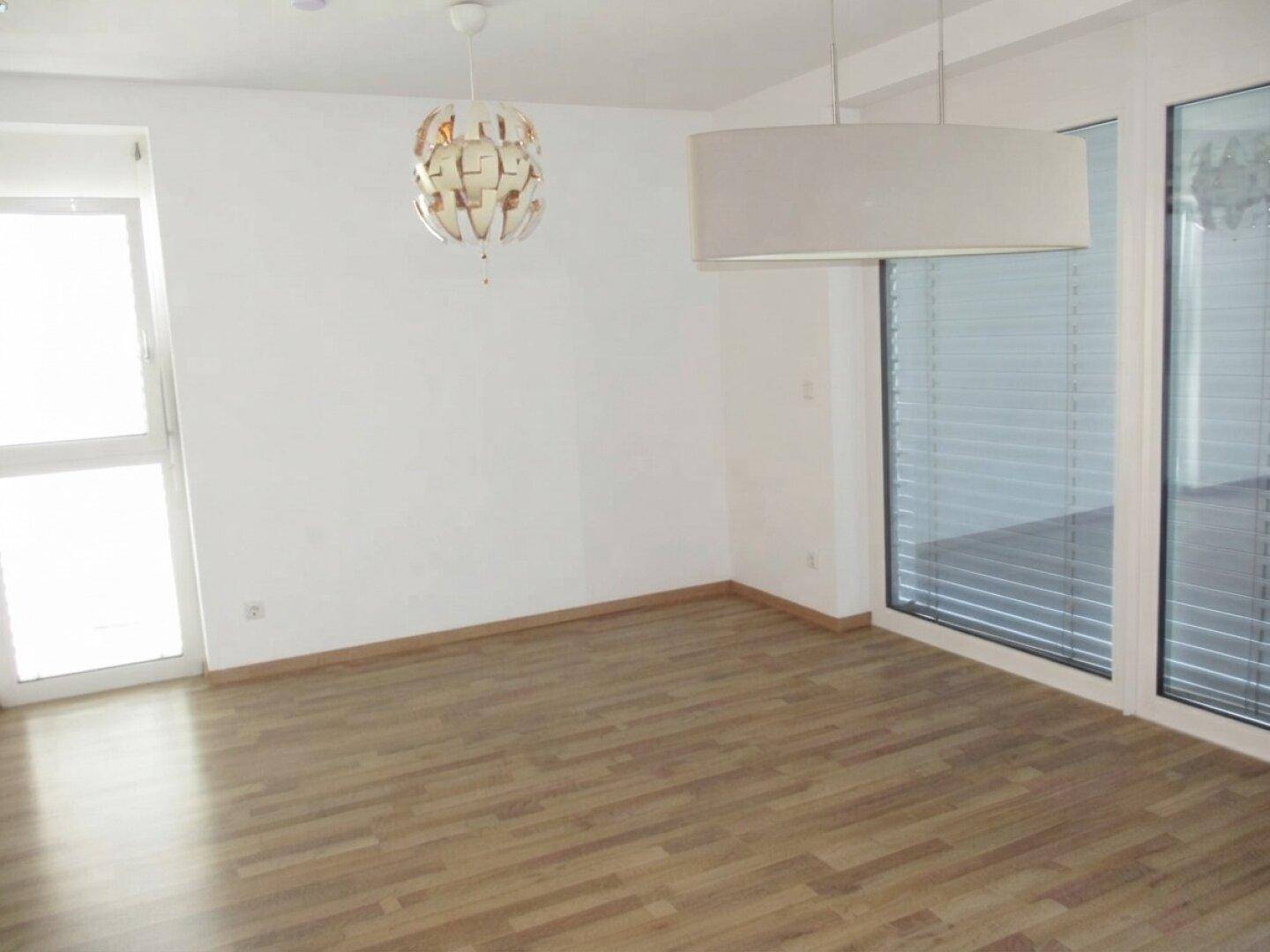 Lichtdurchfluteter Wohnbereich mit Laminatboden, großen Fenstern und Zugang zu einem Außenbereich.