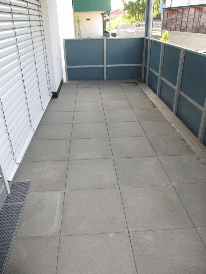 Geräumiger Balkon mit grauen Fliesen und blauer Brüstung, ideal für entspannte Stunden im Freien.